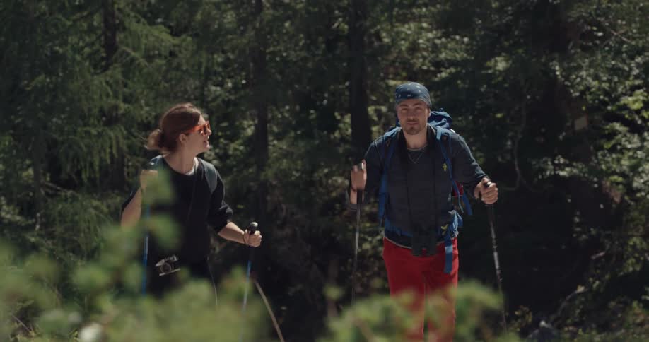 A man and woman uses hiking poles to walk up a hill