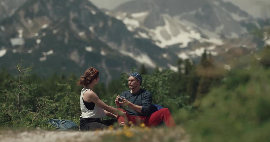 Young couple hiking in the mountains take pictures of themselves while sitting on the ground