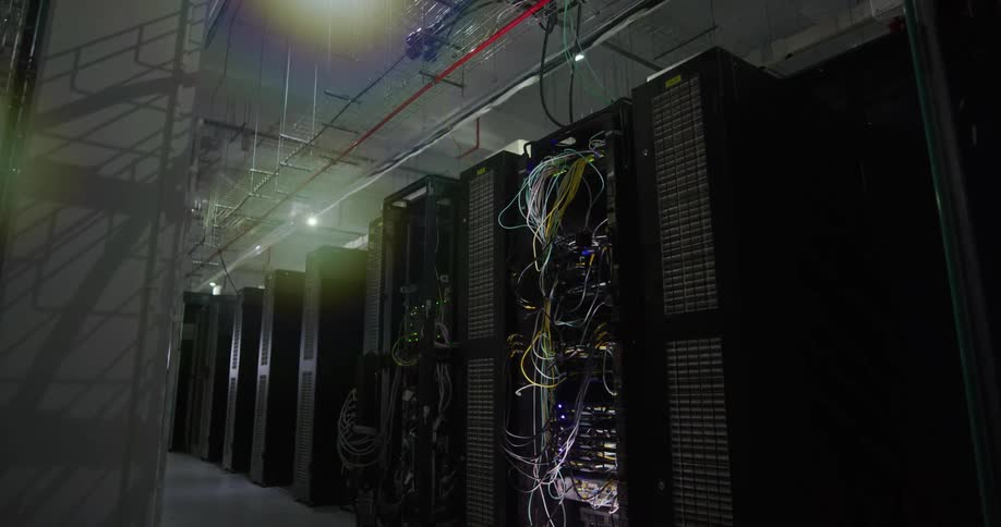 A data center is filled with several tall server racks equipped with numerous wires and cables