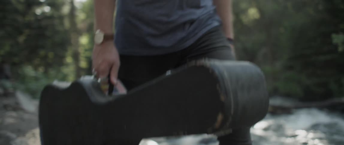 A man carries a guitar case in a forested area