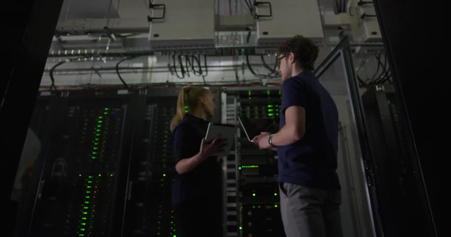 A man and a woman in a room with tablets standing by server racks