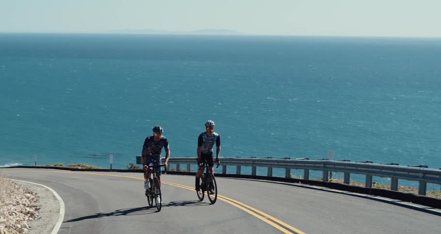A view of two men riding bikes up a road next to the sea