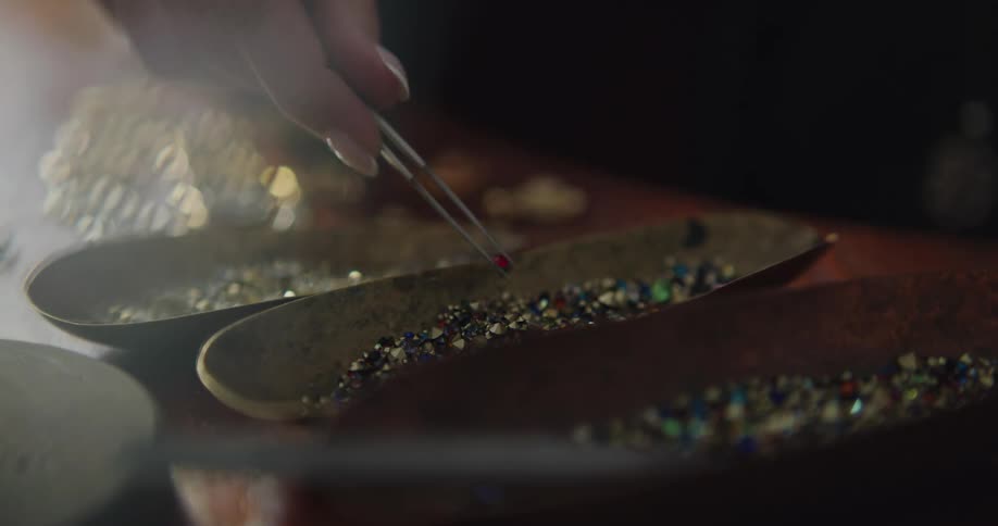 A woman uses a tweezer tool to pick out gemstones from a small plate