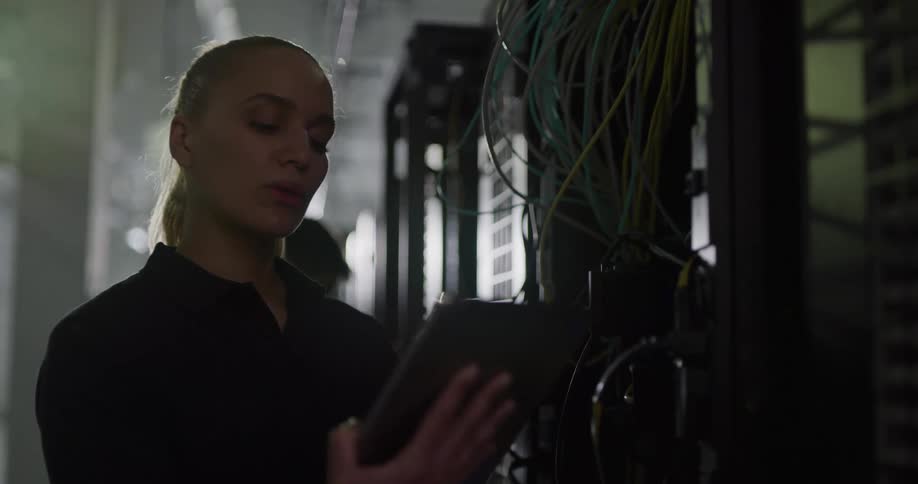 A woman standing in front of a server looks at a tablet as a man behind her works on the equipment