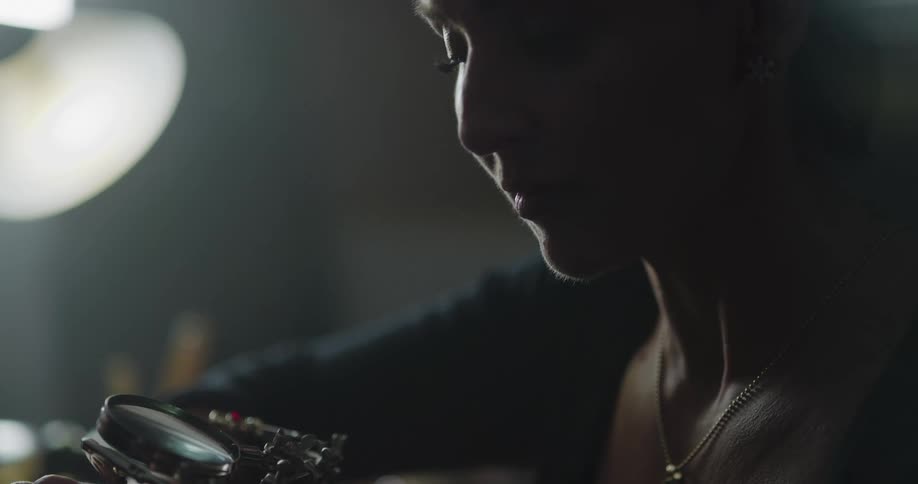 A female jewelry maker peers through a magnifying glass while making a piece of jewelry