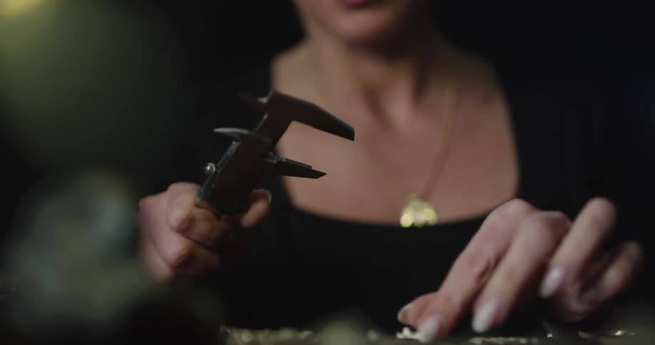 A woman in a room with a necklace using a tool to measure a jewelry piece