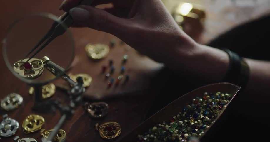 A jewelry designer uses tweezers and a magnifying glass to carefully place a bead