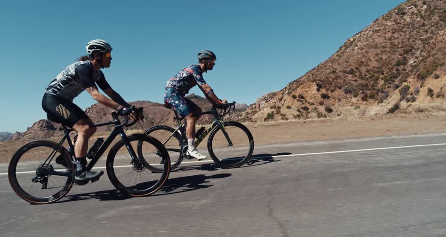 Two people ride bicycles on a rural mountainside road