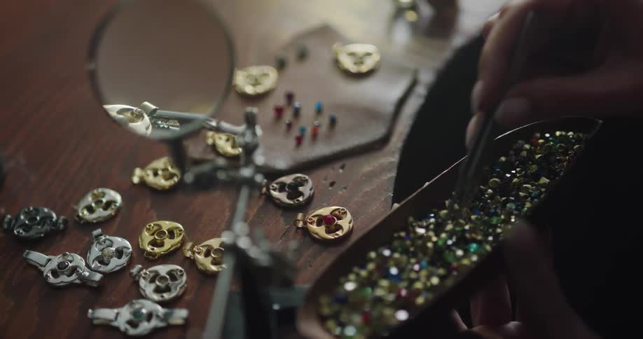 A jeweler uses tweezers to remove small gemstones from a case and place them on a table