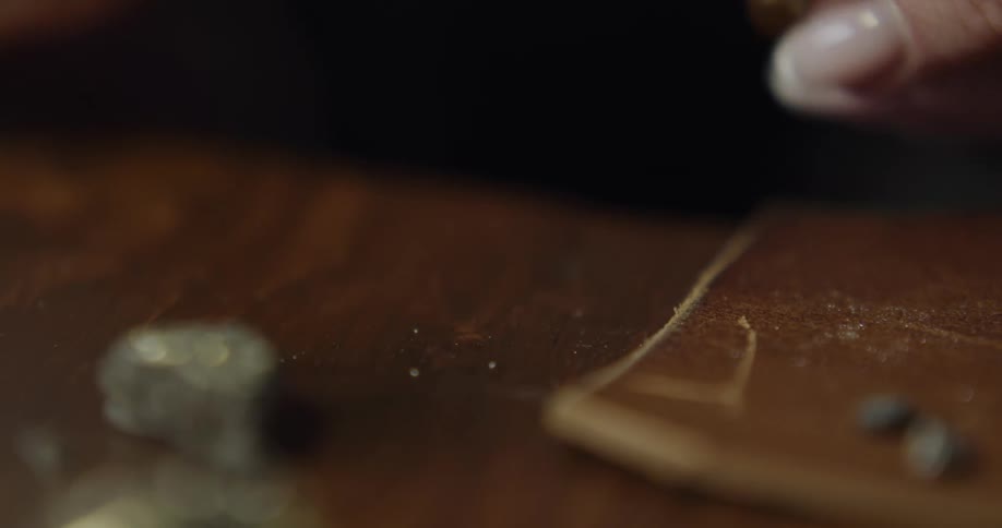 A female jeweler picks up a small golden medallion and a eye loupe