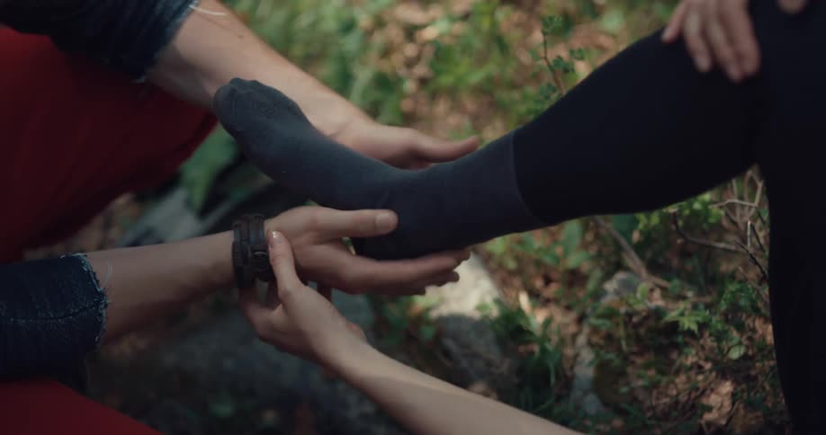 Man helps a woman take off her shoe to check an injured ankle in the forest