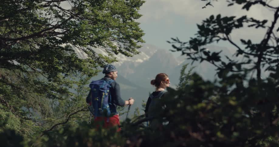 Man and woman carrying backpacks hike through wilderness with mist covered mountains in distance