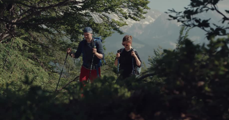 A man and woman in a forest hiking with trees the sky and clouds in the background