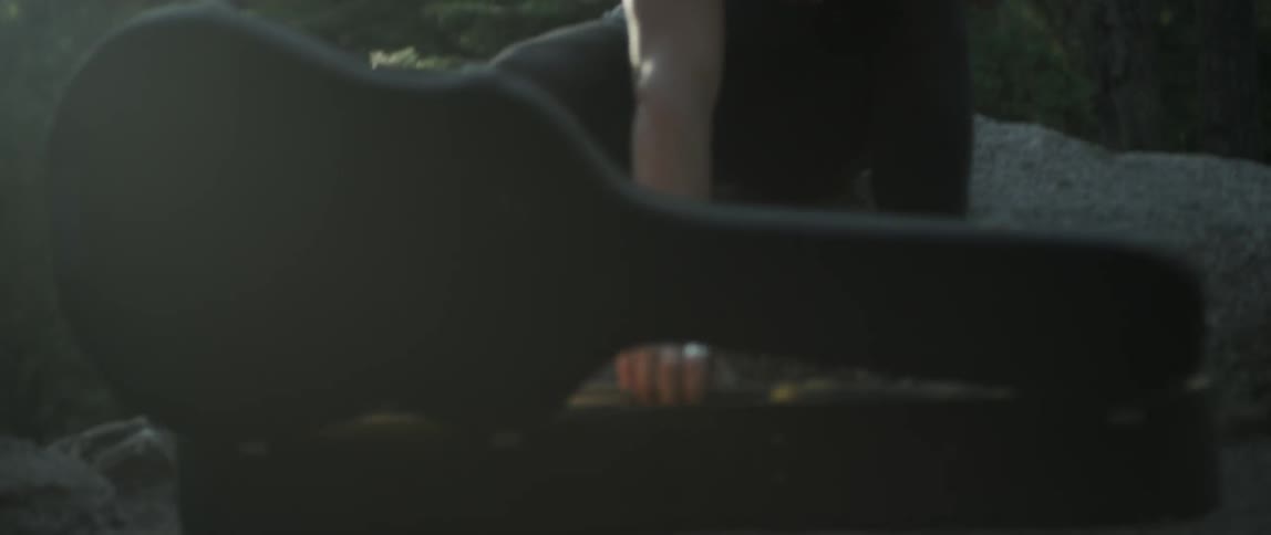 A man sitting outside opens his guitar case and takes out an acoustic guitar