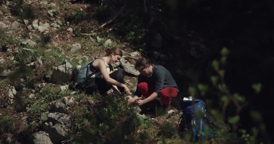 A man bandages the ankle of a woman on a rocky slope in the wilderness during the day