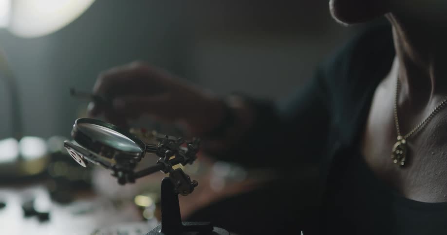 A jewelry designer looks at beads under a magnifying glass