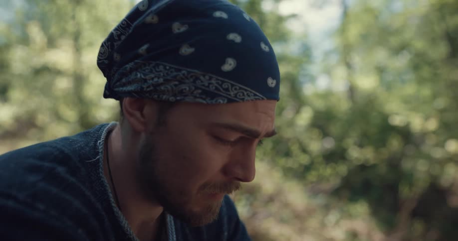 A man in a forest takes off his bandanna and looks in to the distance