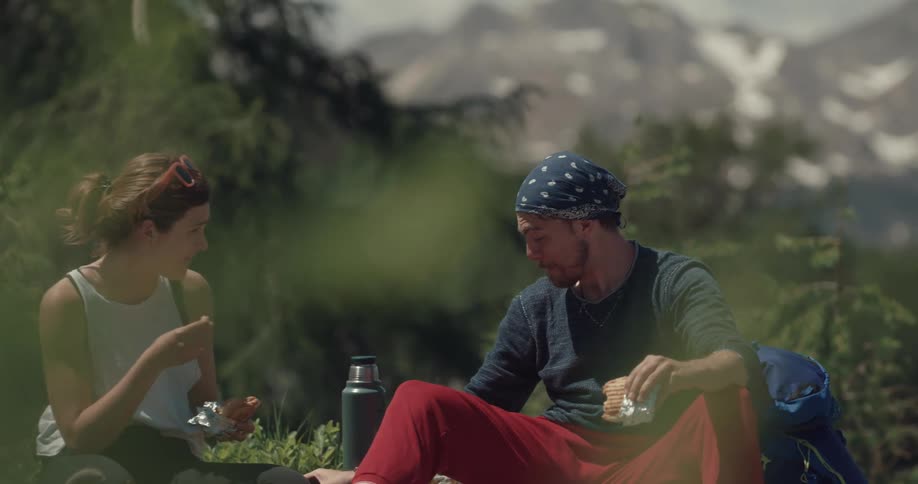 A man and woman sit outside in the wilderness and talk and eat and drink