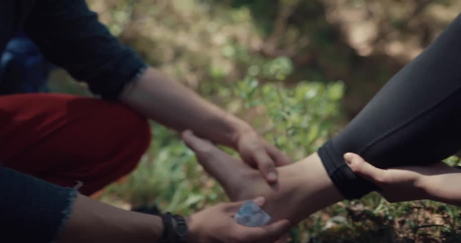 A man wraps the wound of a friend on the ground in a forest during the day