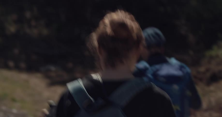 A man and woman with backpacks hiking with trees in the background