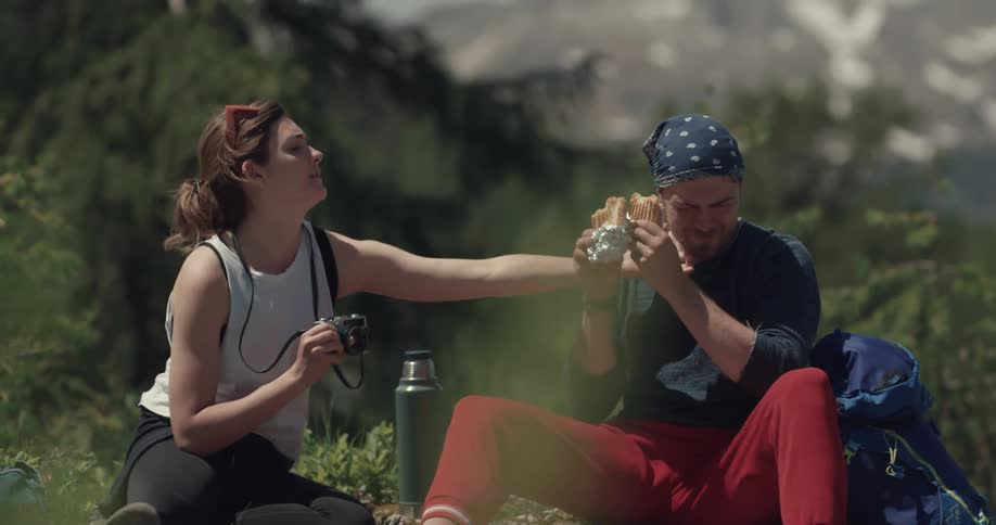 Man laughs while sitting near a forest as a woman takes his photo
