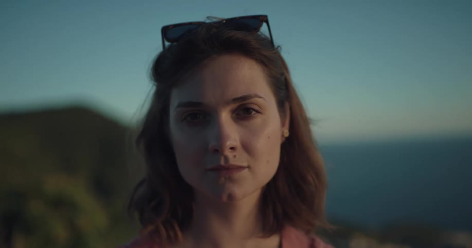 A woman staring off into the distance turns her head to look at the camera