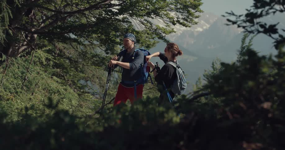 A man and woman with backpacks hiking with trees in the background