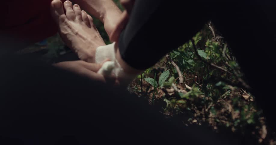 A person is putting a white bandage on the ankle of another person