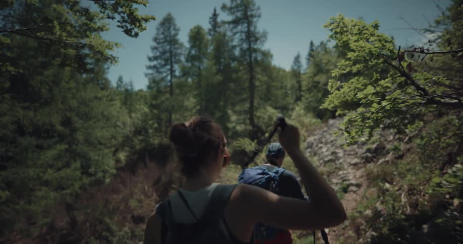 A man and woman use hiking poles to walk a mountain pathway