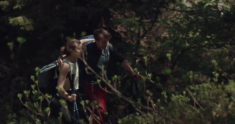 A man helps a woman as she limps while hiking