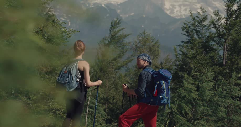Man and woman with backpacks walk up a hill using trekking poles