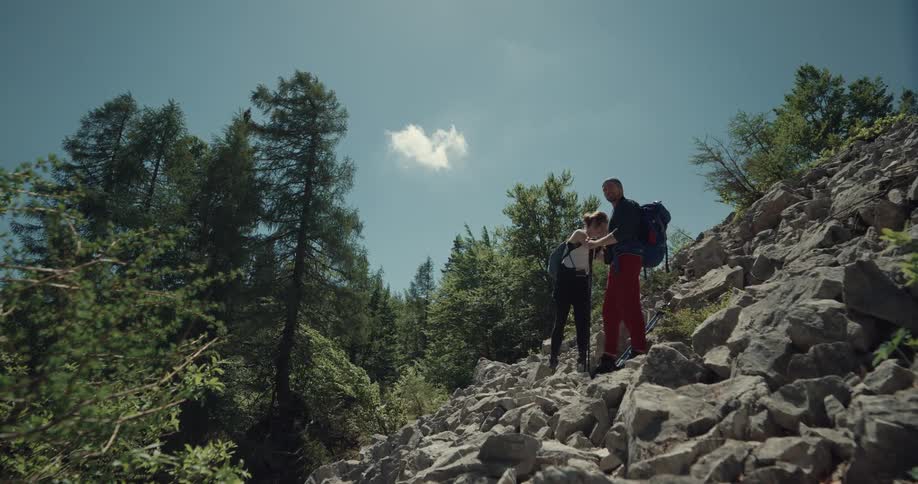 A man and woman in a forest hiking with trees the sky and clouds in the background