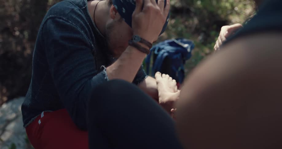 Man uses a kerchief to wrap a womans injured foot in the forest