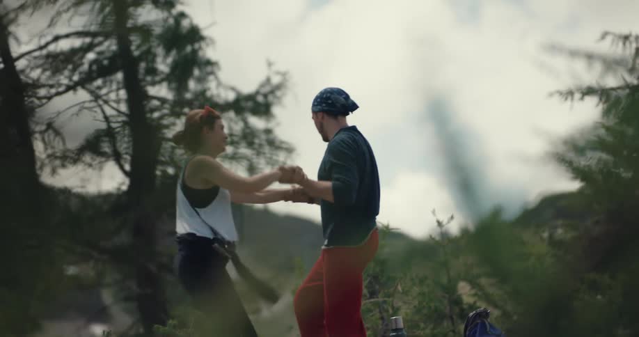A man and woman stand up and gather their hiking supplies in a rural woodland area