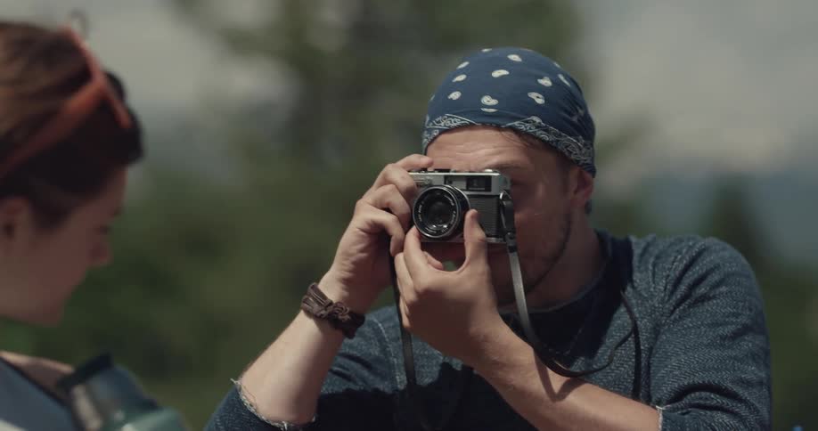 Man wearing a kerchief on his head takes a photo of a woman holding a thermos