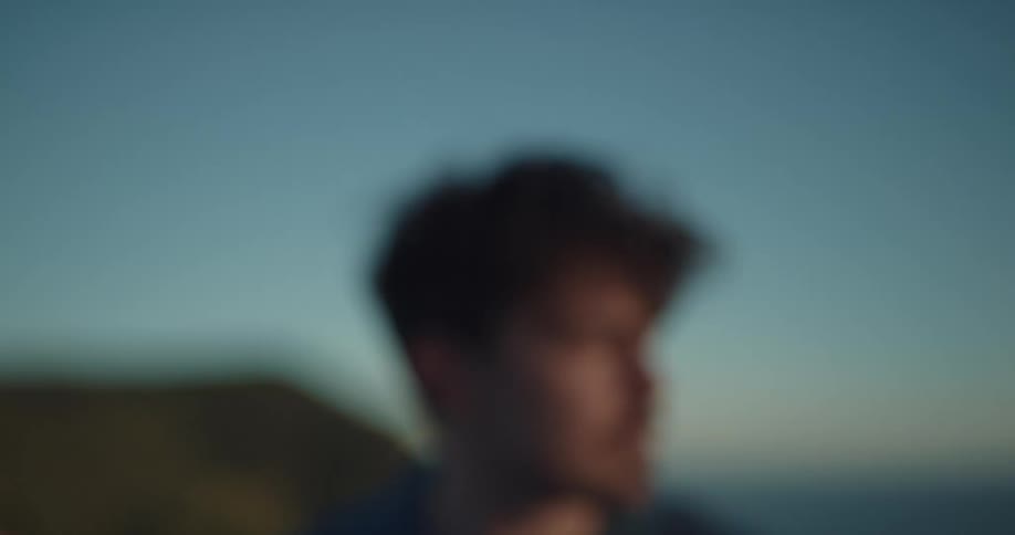 A man looks out over the wilderness before turning to grin into the camera