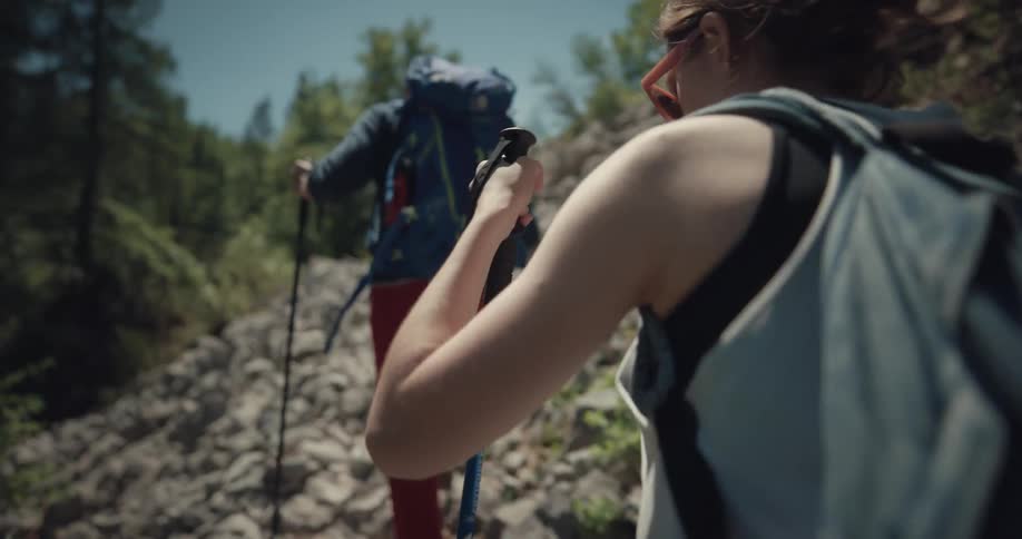 A woman and man hike across rocky terrain in a forest during the day
