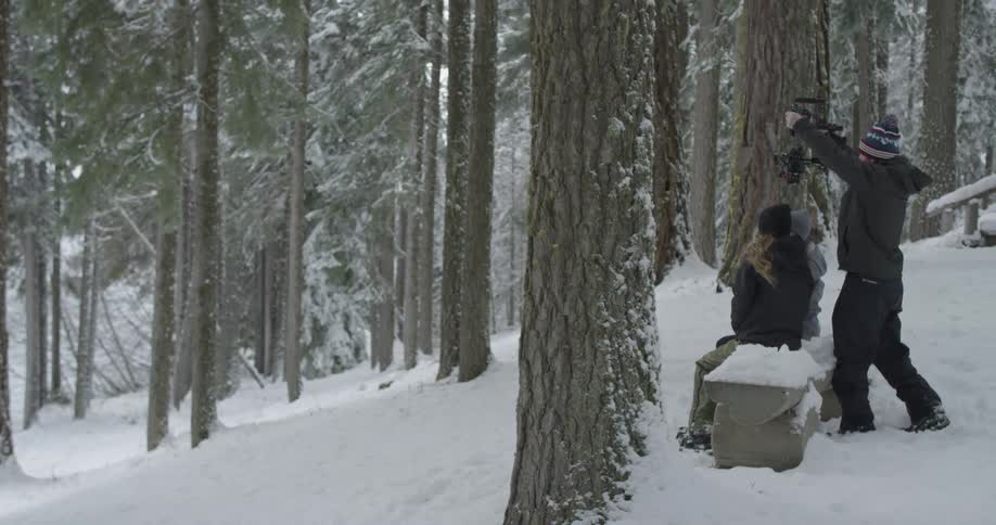 Two people sitting at a bench while another holds a camera over their heads