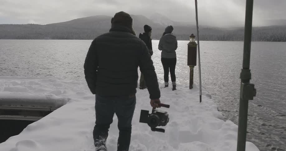 Three people stand on an icy pier overlooking a mountain lake