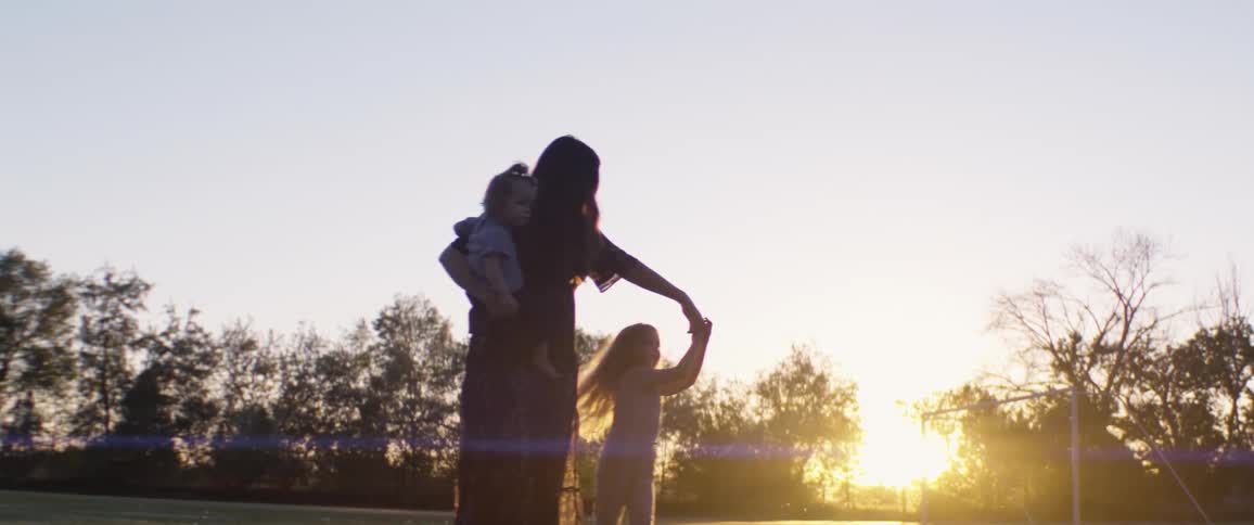 Mother holding a baby in her arms and twirls her child while walking in a field