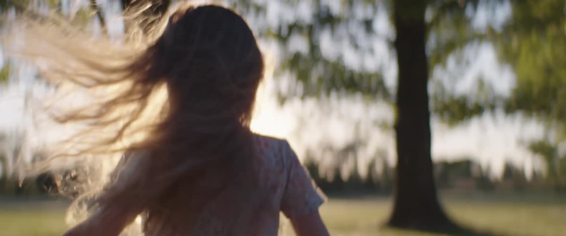 A young girl with long hair smiling and running outside in the park during summer