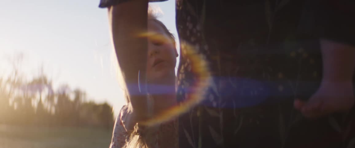 A mother running her hand through her daughters long hair outside on a summer day