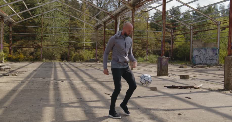 A man does ball tricks with a soccer ball in a rural fenced in area