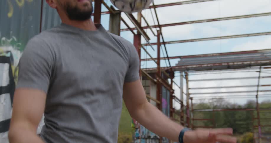 A man juggles a soccer ball using his head and shoulders while standing in a ruined building during the day