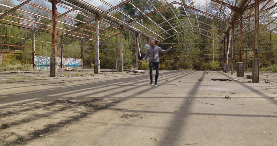 A male stands beneath an empty structure while juggling a soccer ball with his feet