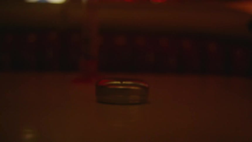 A person in a room with a ring releasing a silver cylinder that moves across a table towards another person