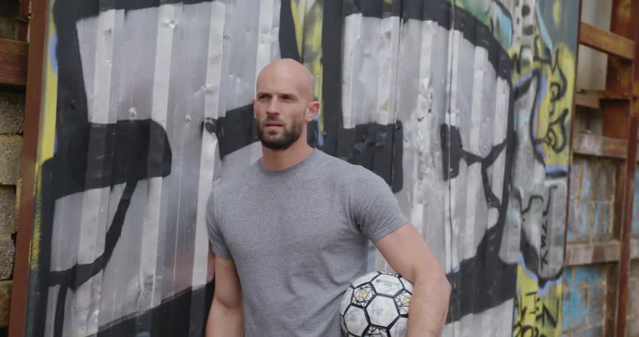 A man is standing by a wall and holding a soccer ball