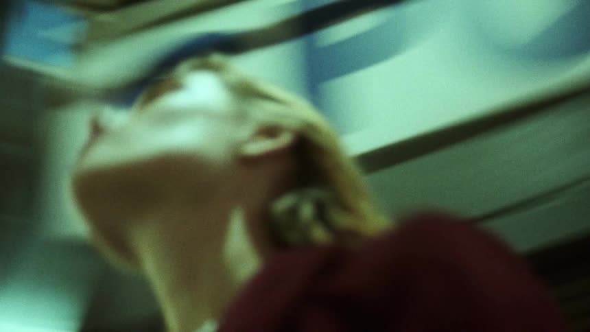 A woman looks upwards at several tall buildings as the camera spins around her
