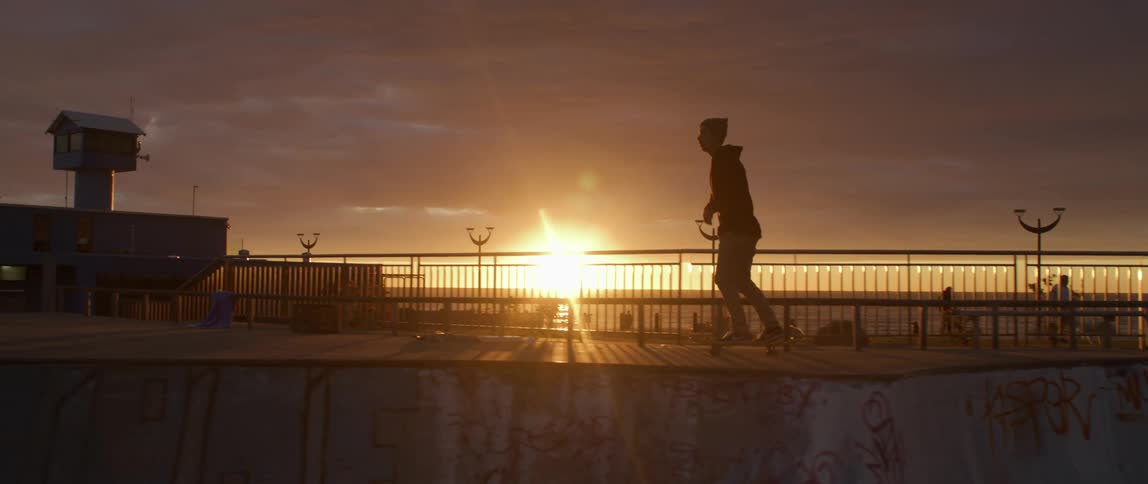 A silhouette of a man skating on a skateboard with a sunset the sky and clouds in the background