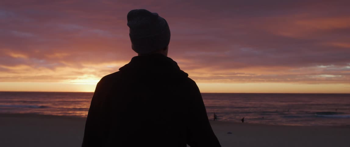 A man is standing by the coast of a beach at dusk